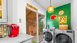 Eine Küche mit Kaffeemaschine, Waschmaschinen und einer grünen Wand mit Kunstwerken.