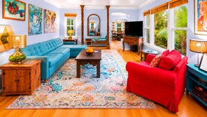 Ein Wohnzimmer mit blauem Sofa, rotem Sessel, Couchtisch aus Holz und bunten Teppichen.