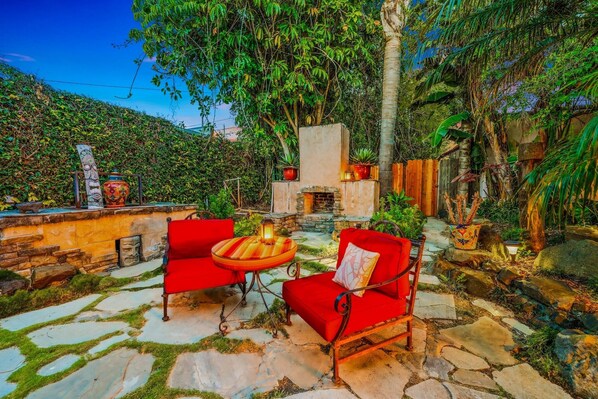 A stone patio with red chairs and a table, surrounded by lush greenery and a stone wall. - 25%OffOct 22-25 Great Reviews Mins 2 Beach Jacuzzi (Ventura)