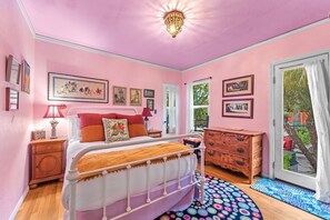 Une chambre à coucher décorée dans des tons roses, avec un lit, une commode et une vue sur le jardin grâce à une porte coulissante.