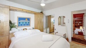 A hotel room with a bed, a ceiling fan, a painting, and a wardrobe.