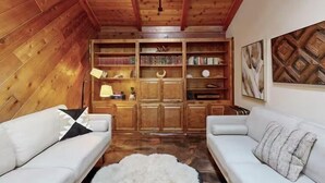 A cozy room with wooden walls and ceiling, a white sofa, a bookshelf, and a small table with a lamp.