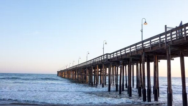A pier extending into the ocean with a wooden walkway and street lamps.