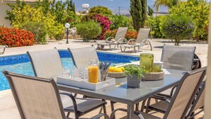 A poolside dining area with a table set for four, surrounded by lounge chairs.