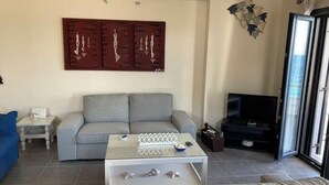 Een woonkamer met een grijze bank, een witte salontafel en een televisie.