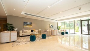 Un hall d’entrée spacieux au design moderne, comprenant un grand espace salon avec des canapés et des poufs, une table basse et des œuvres d’art accrochées aux murs.