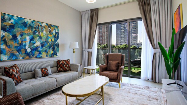 Un salon moderne avec un canapé gris, un fauteuil à motifs, une table basse blanche et un grand tableau abstrait.