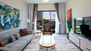 Un salon moderne avec un canapé, une table basse et un téléviseur. Un grand tableau abstrait orne le mur, et la fenêtre offre une vue sur l’extérieur.