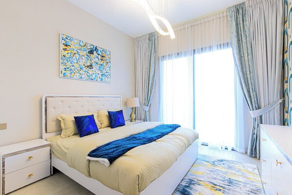A modern bedroom with a large bed, a nightstand, a dresser, and a painting on the wall.