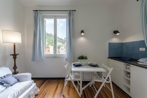 Ein gemütlicher Raum mit Esstisch, weißen Stühlen, einer Lampe, einem Fenster mit Vorhängen und Blick auf Gebäude.