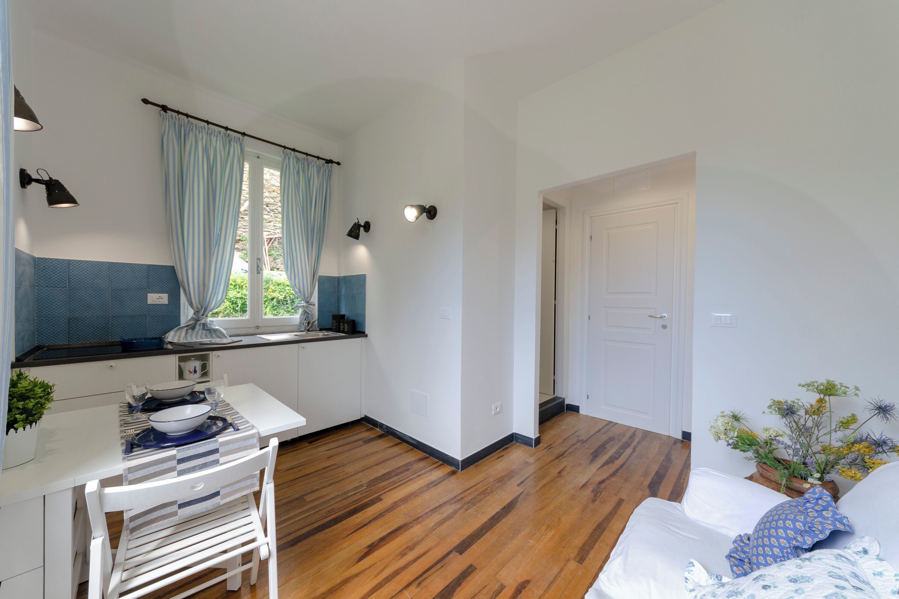 A compact kitchen with a dining area, a window with curtains, and a door leading to another room.
