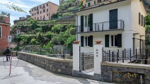 Un edificio blanco con un balcón, pared de piedra y una escalera de piedra que lleva a la entrada.