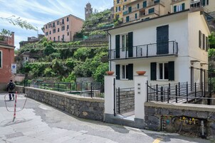 Um edifício branco com varanda, parede de pedra e escadaria de pedra que leva até ele.