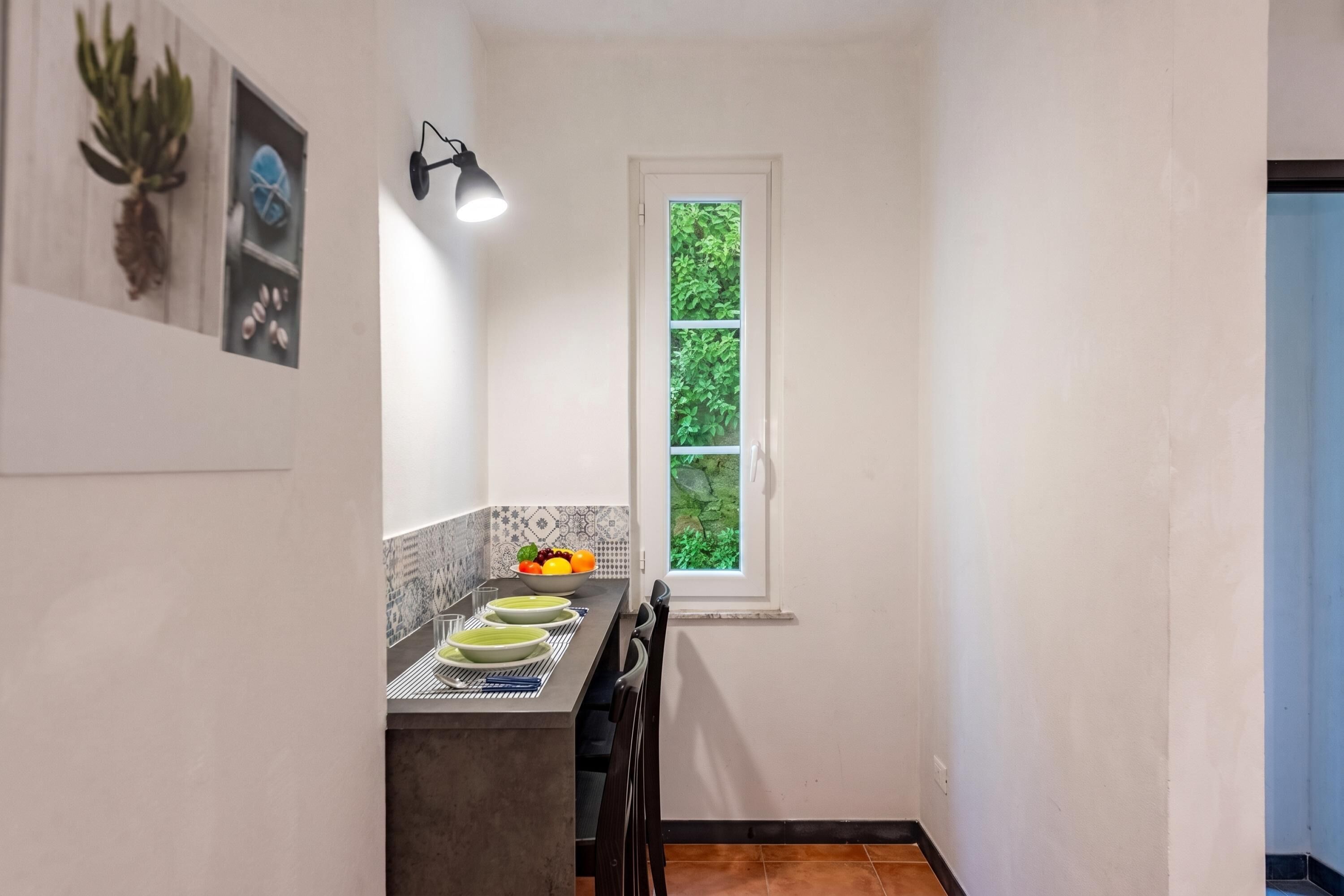 A kitchen with a window, a plant, and a bowl of fruit on the counter.