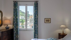 Una habitación de hotel con una cama, una mesita de noche con lámpara, un aparador y una ventana con cortinas.