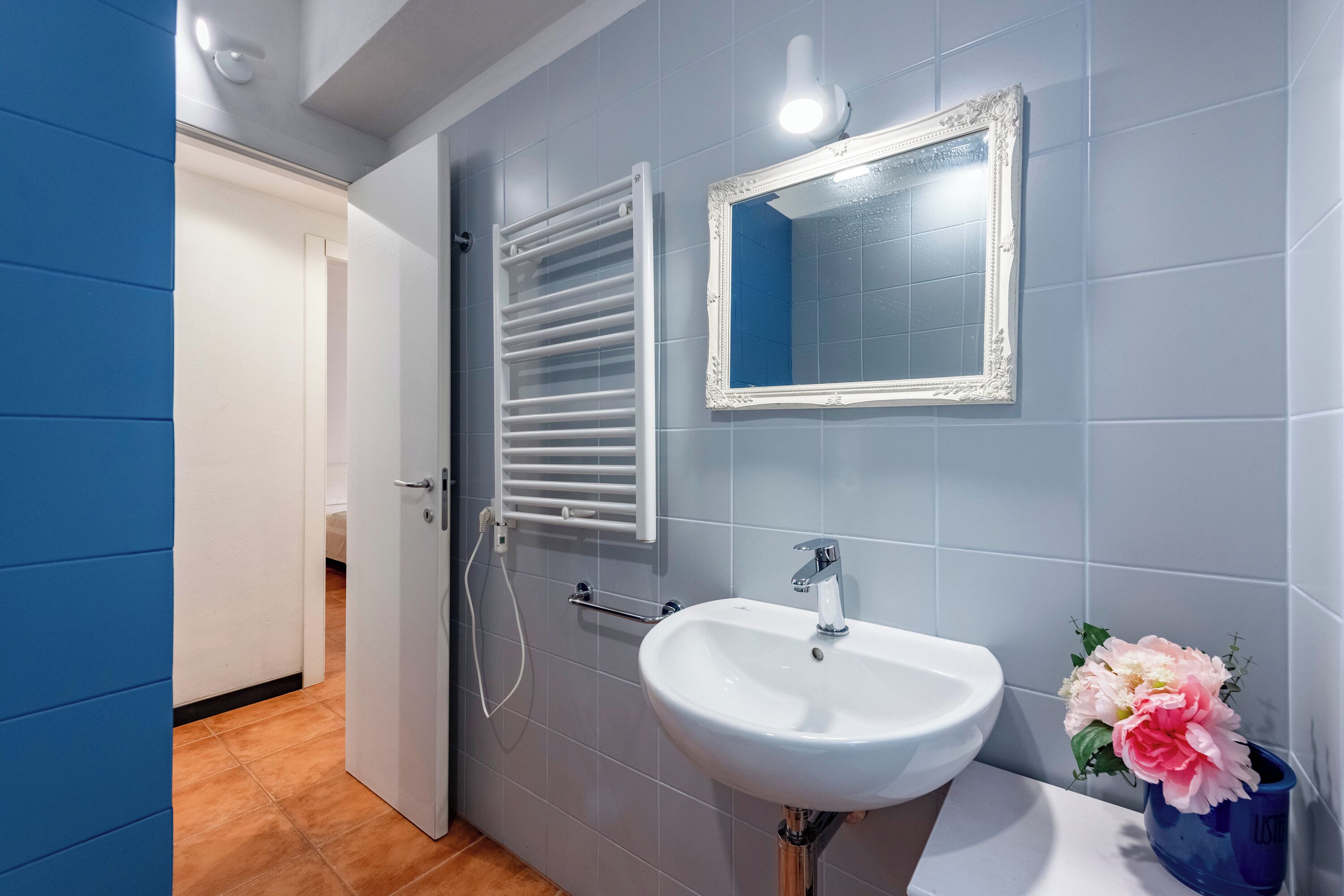 Un baño con lavamanos blanco, un espejo y un perchero para toallas.