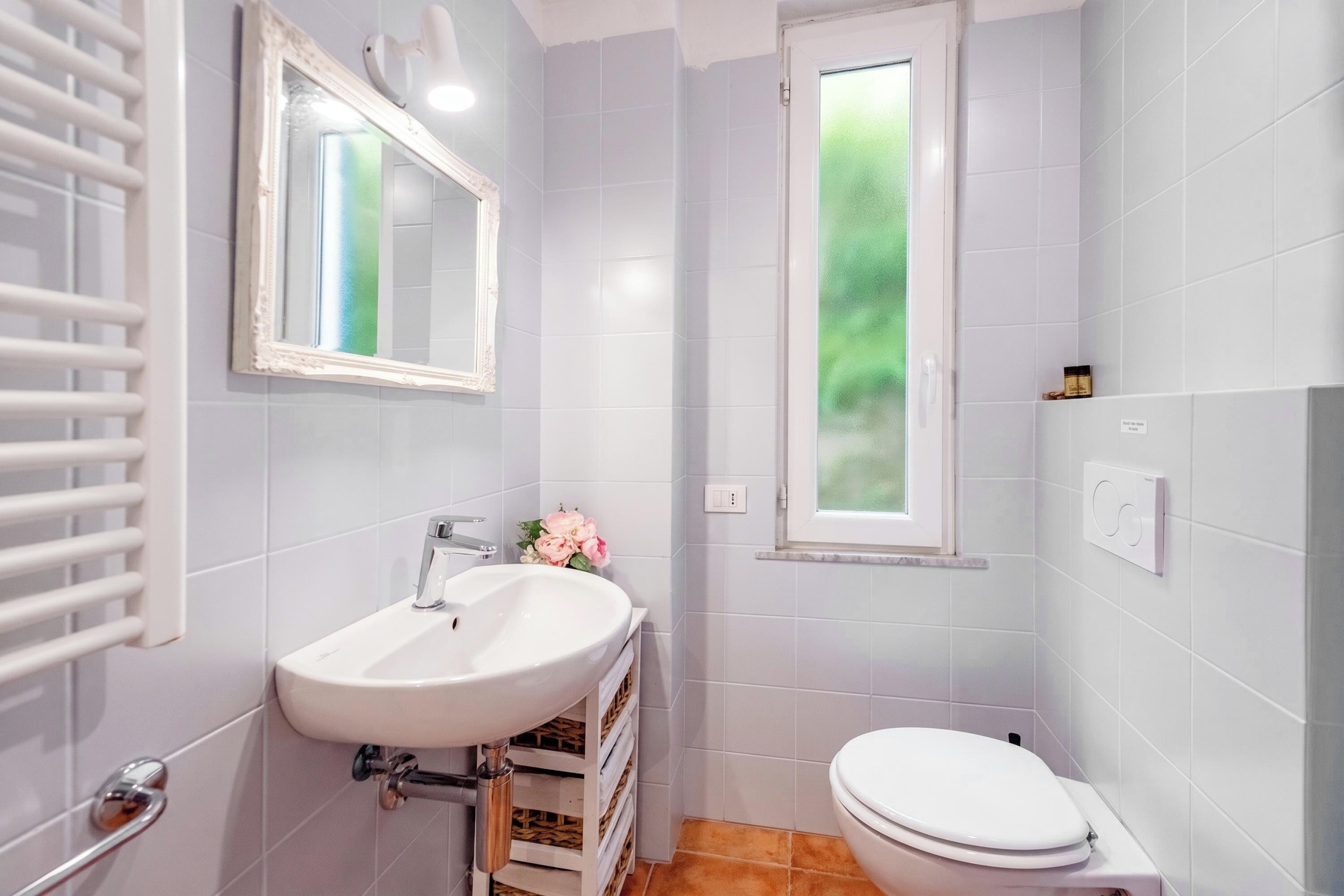 A bathroom with a white sink, a toilet, a mirror, and a window.