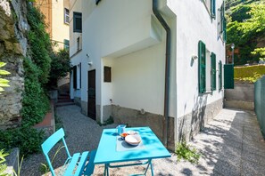 A courtyard with a table and chairs, a stone wall, and a building with green shutters. - Vernazza Apartments (Vernazza)