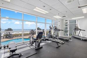 A gym with exercise equipment and a view of a beach and pool. - Palacio 1405 (Pensacola)