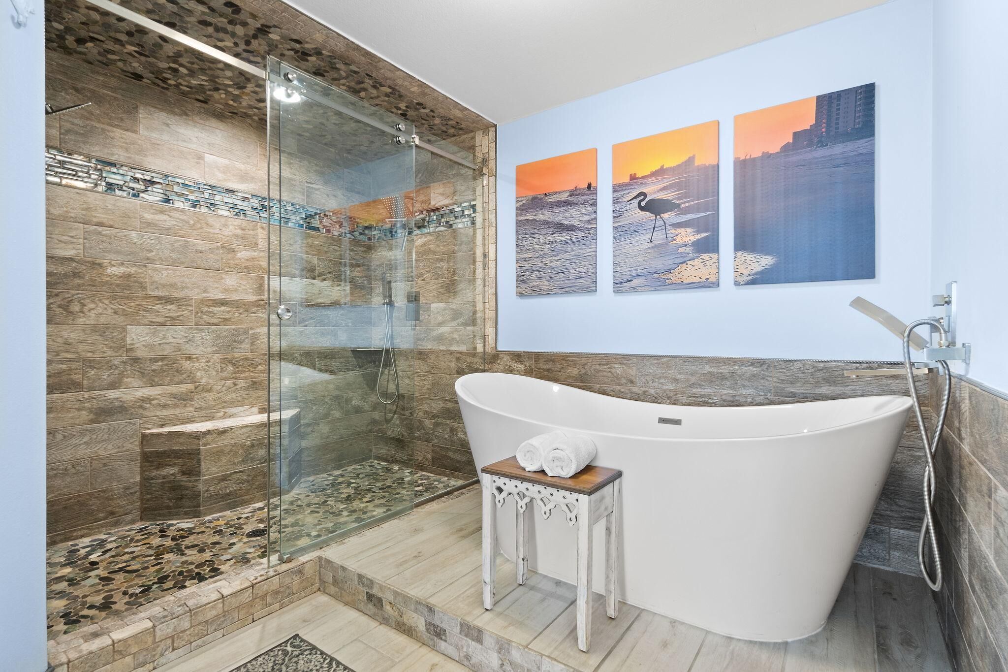 Een moderne badkamer met een glazen douchecabine, een vrijstaand bad en drie zonsondergangschilderijen aan de muur.