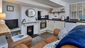 A modern living room with a fireplace, a television, a sofa, and a kitchen area with a microwave and kettle. - Cottage in Whitby Near Stunning Beaches (Whitby)