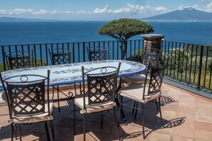An outdoor dining area with a table and chairs, a view of the sea, and a mountain in the background. - Torre Cangiani (Massa Lubrense)