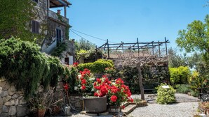 A stone building with a balcony, surrounded by lush greenery and red flowers. - Torre Cangiani (Massa Lubrense)