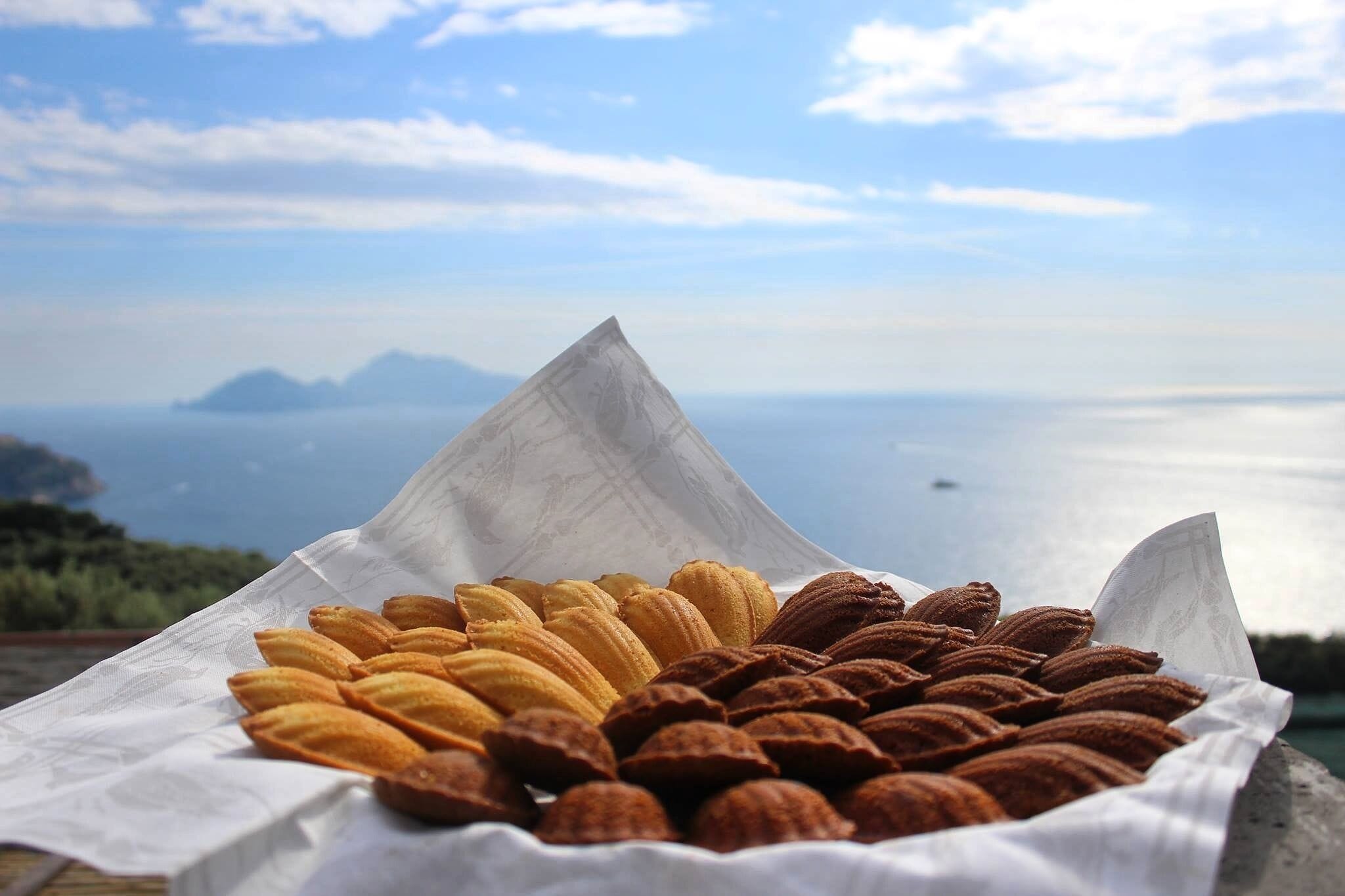 Un plateau de pâtisseries, avec en arrière-plan une vue magnifique sur la mer et les montagnes.