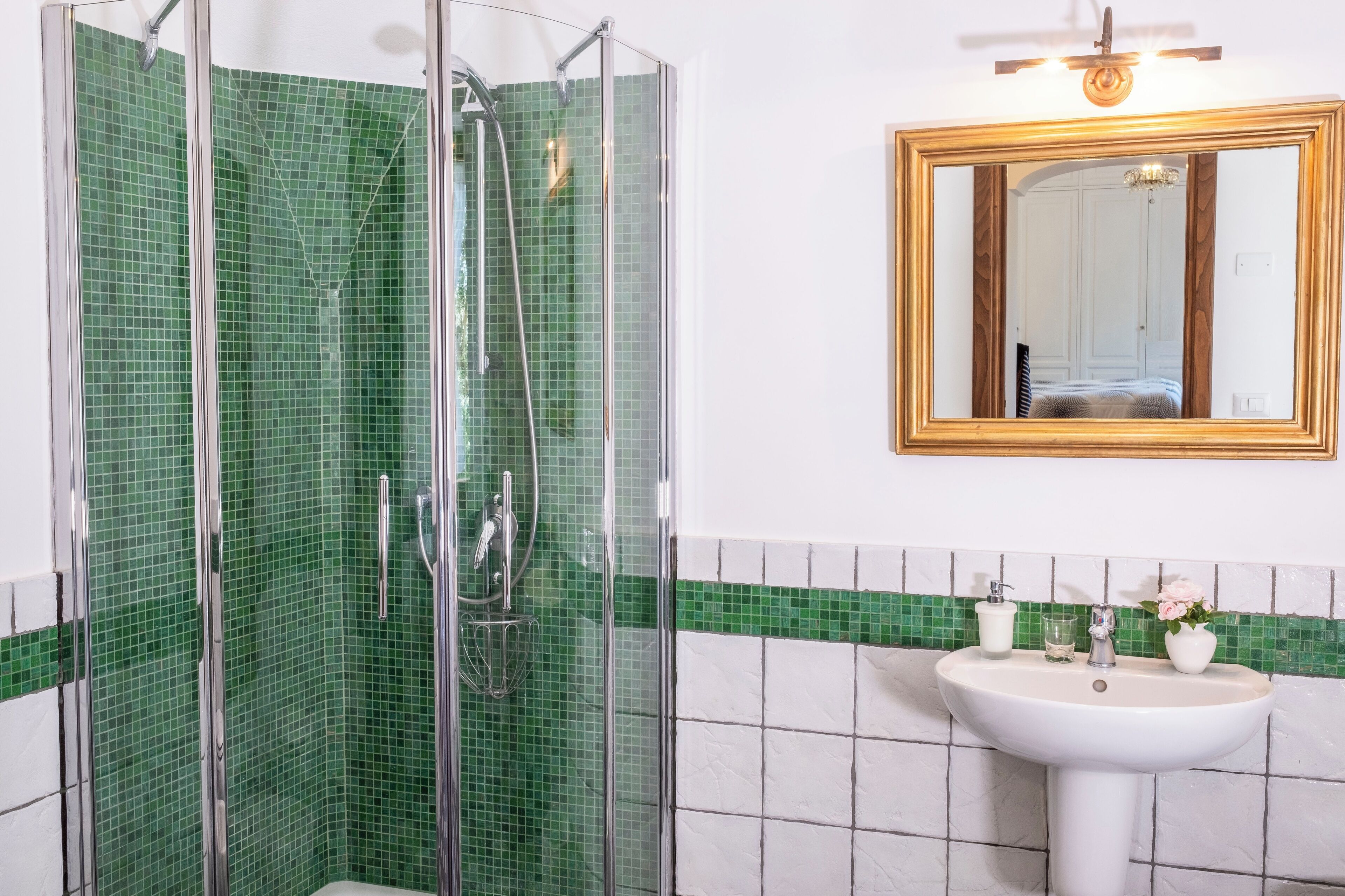 Une salle de bain avec une douche à parois de verre, un lavabo blanc et un miroir avec un cadre en bois.