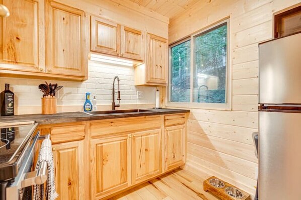 Cocina de cabaña de madera con un refrigerador de acero inoxidable, armarios de madera y una ventana con vista a un bosque.
