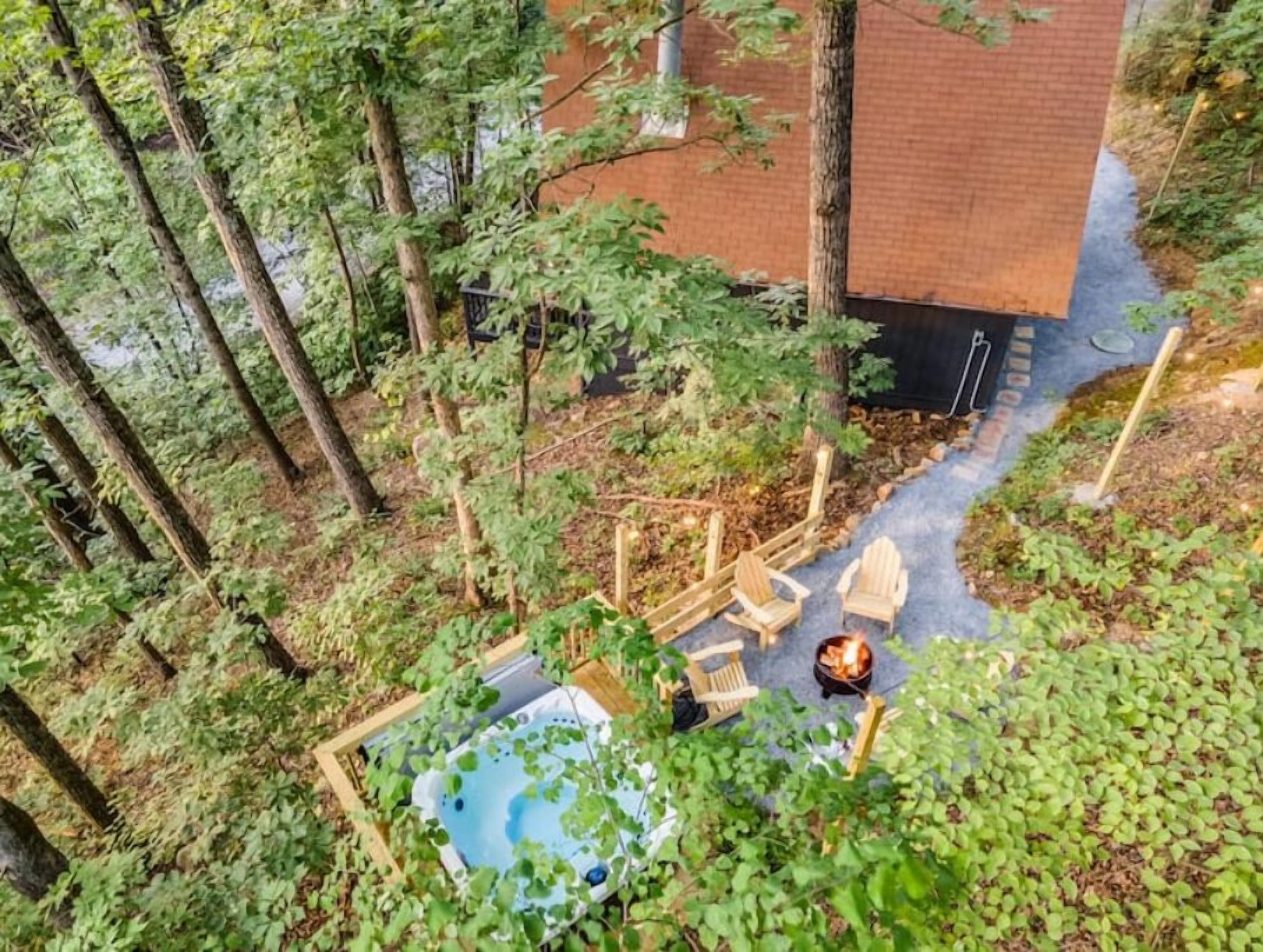 A backyard with a hot tub, wooden chairs, and a fire pit.