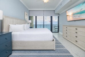 A bedroom with a large bed, a dresser, a nightstand, a painting, and a balcony with a view.