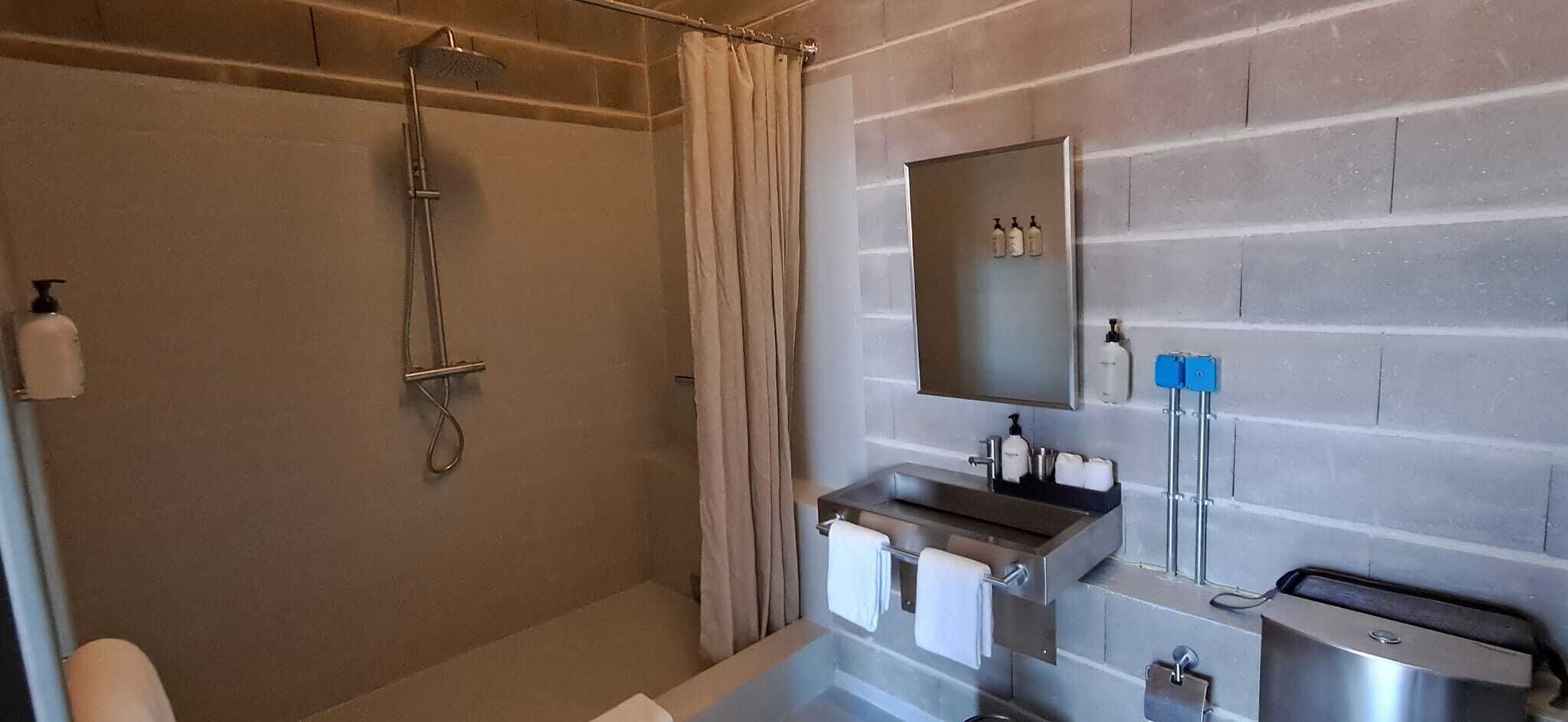 A modern bathroom with a glass-enclosed shower, a vanity with a sink and mirror, and toiletries on the wall.