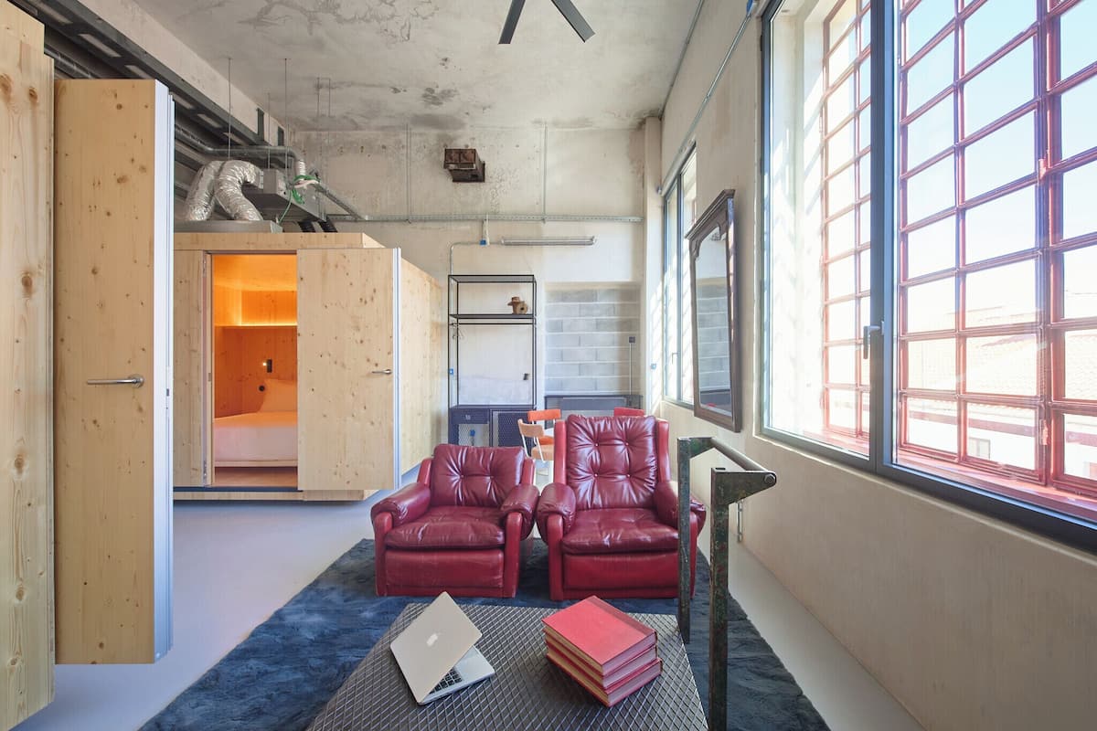 Una habitación con dos sillones de cuero rojo, una computadora portátil y una pila de libros sobre una alfombra azul.