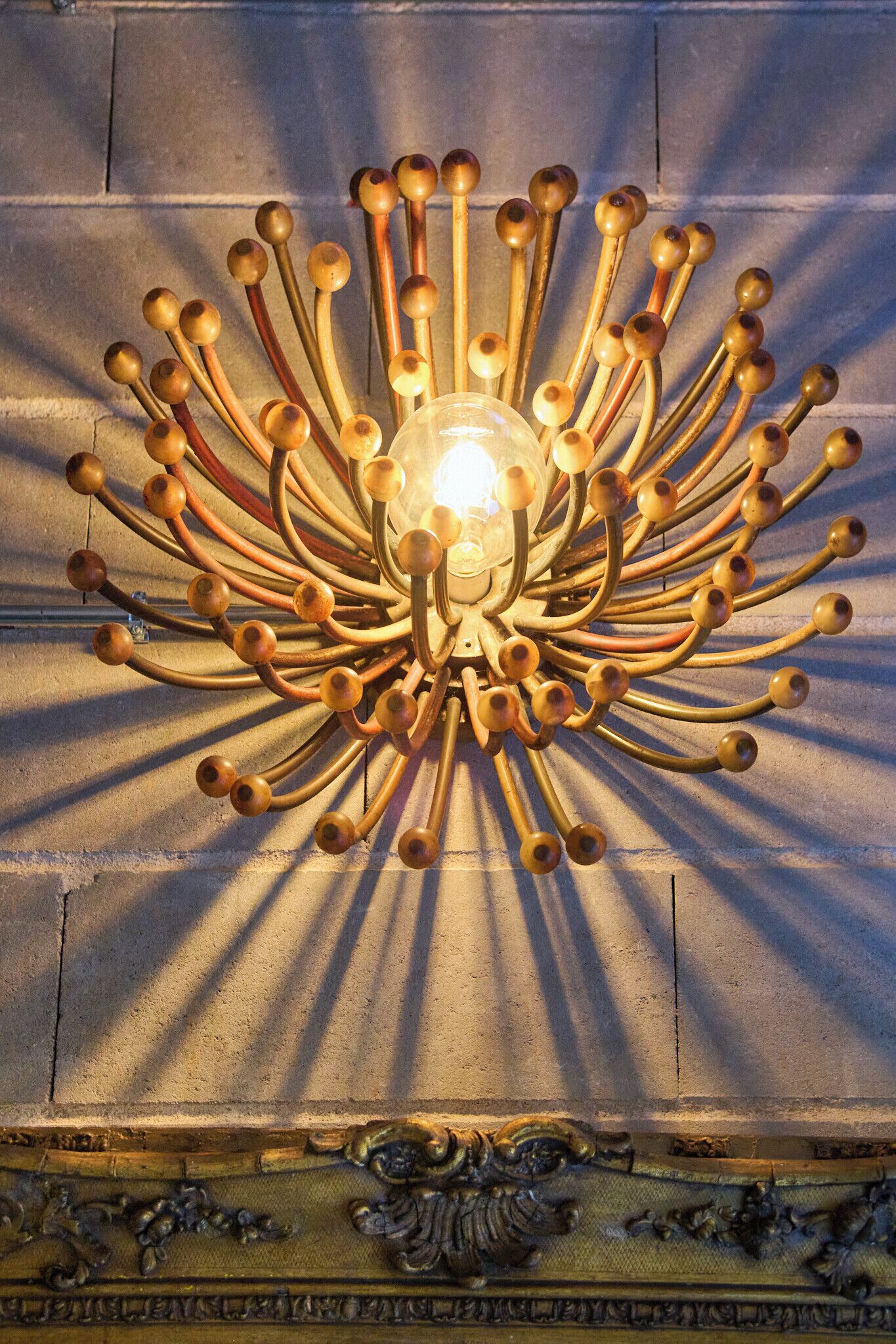 Un candelabro con múltiples brazos y bombillas esféricas frente a una pared con textura.