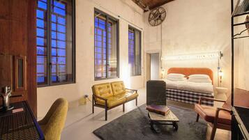 A room with a bed, a yellow sofa, a chair, a table, and large windows.