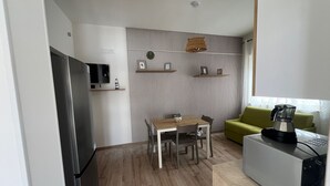 A compact kitchen with a refrigerator, a coffee maker, and a dining table with chairs.