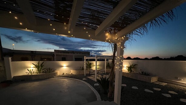 A covered outdoor patio area with string lights, seating, and planters.