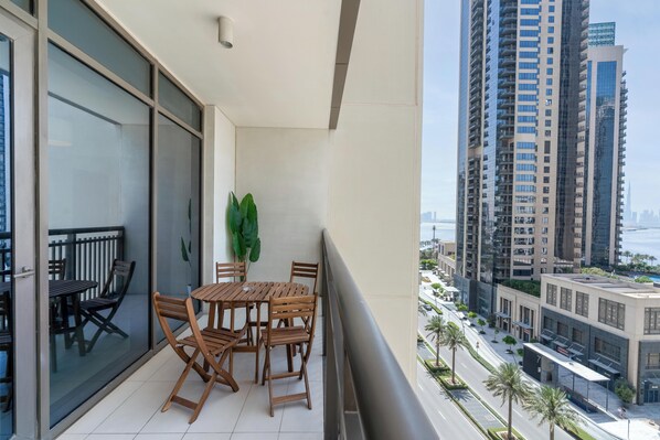 A balcony with a table and chairs, a potted plant, and a view of tall buildings and a road. - Lux BnB Creek Side 18 (Dubai)