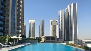 Una piscina con sillas de descanso y sombrillas, rodeada de edificios altos.