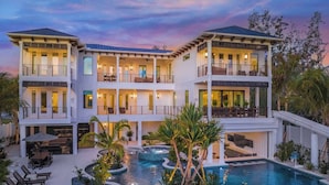 Una casa de varios pisos con piscina, mobiliario de exterior y una escalera que conduce a los niveles superiores.