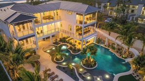 Un hotel de varios pisos con piscina, mobiliario exterior y palmeras.
