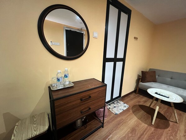 Habitación de hotel con un aparador de madera, un espejo redondo, un sofá gris y una mesita blanca.