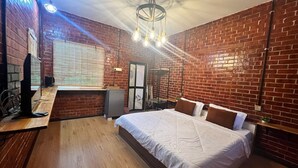 A bedroom with a brick wall, a wooden floor, a bed with white bedding, a desk with a computer, and a ceiling light fixture. - Capital O 91152 Jerot Dusun Campsite (Yan)