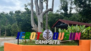 A campsite sign with colorful lettering and a logo, surrounded by greenery and trees. - Capital O 91152 Jerot Dusun Campsite (Yan)