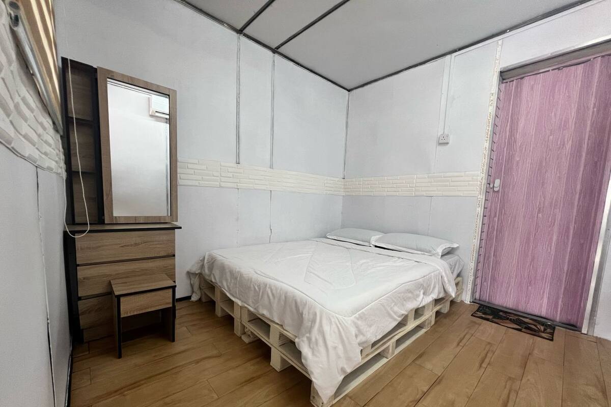 A bedroom with a bed, a wooden dresser, a mirror, and a door.