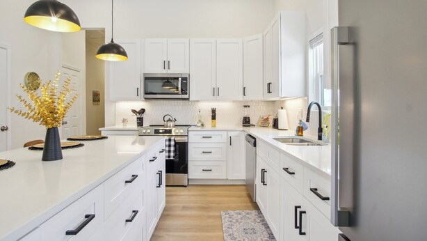A modern kitchen with white cabinetry, a central island, stainless steel appliances, pendant lighting, and a decorative vase.