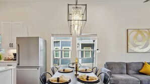 A modern kitchen with a stainless steel refrigerator, a dining table set with plates and napkins, and a chandelier above.