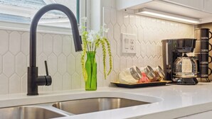 A modern kitchen with a stainless steel sink, a black faucet, a green vase with flowers, and a coffee maker.