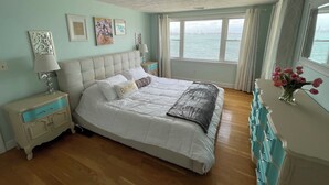 A bedroom with a large bed, a nightstand, a dresser, and a view of the water. - Spectacular Ocean Sunsets I Pet Friendly (Weymouth)